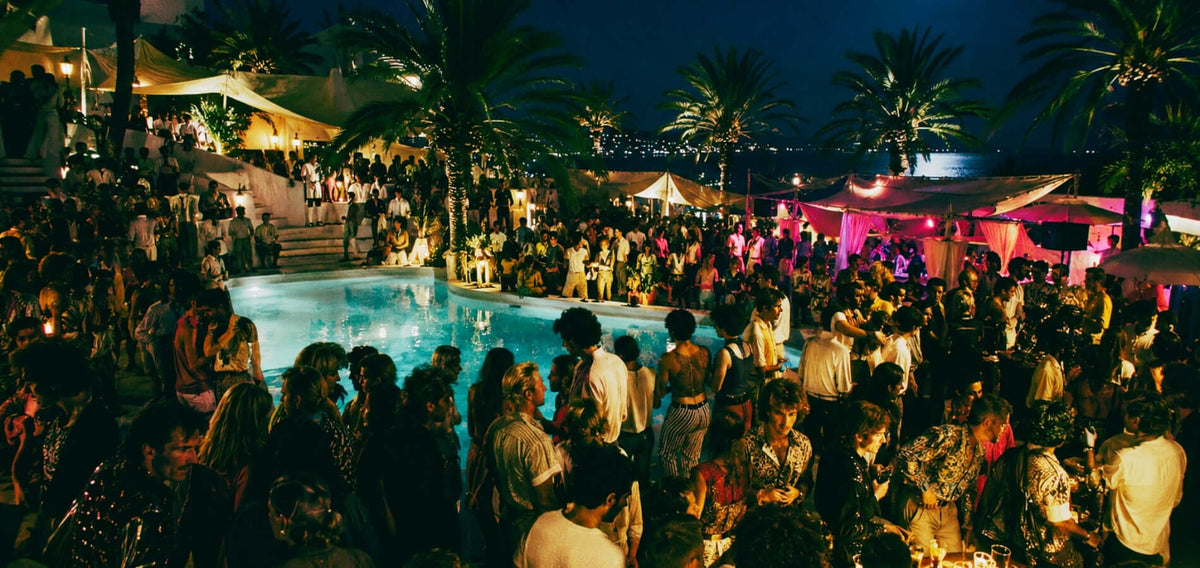 1980s Ibiza open-air club scene with a swimming pool, palm trees and dancers beneath the night sky.