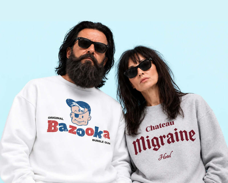 Couple wearing stylish sweatshirts, one featuring 'Bazooka Bubble Gum' and the other 'Chateau Migraine Hotel'.