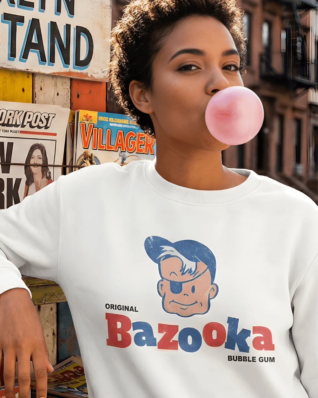 Person wearing a BAZOOKA JOE SWEATER | RETRO BUBBLEGUM CLUB, blowing pink bubblegum in a vintage setting.