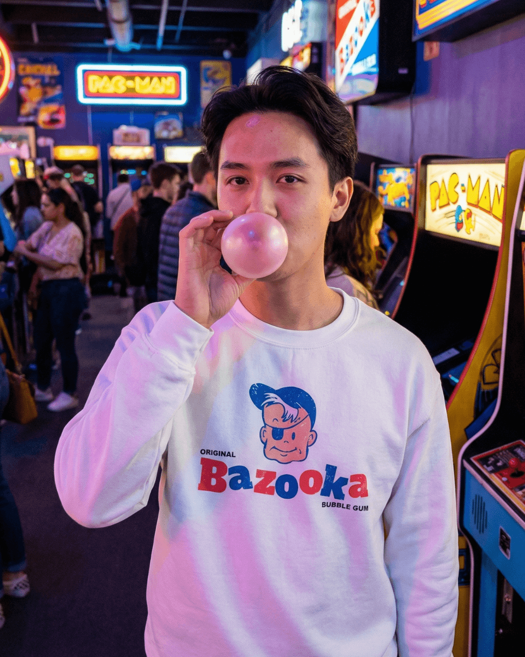 BAZOOKA JOE SWEATER | RETRO BUBBLEGUM CLUB worn by a person blowing a bubble in an arcade.