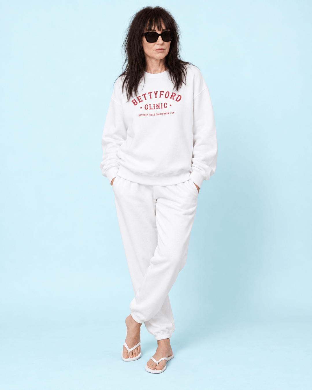 Woman wearing a stylish white Betty Ford Clinic Heavy Sweater with black sunglasses and relaxed-fit pants.