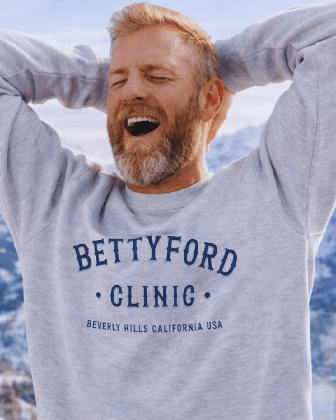 Man wearing a BETTY FORD CLINIC HEAVY SWEATER with a mountain backdrop.