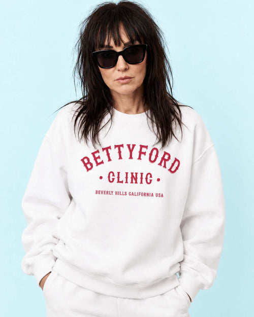 Woman wearing a white Betty Ford Clinic Heavy Sweater with red lettering and sunglasses.
