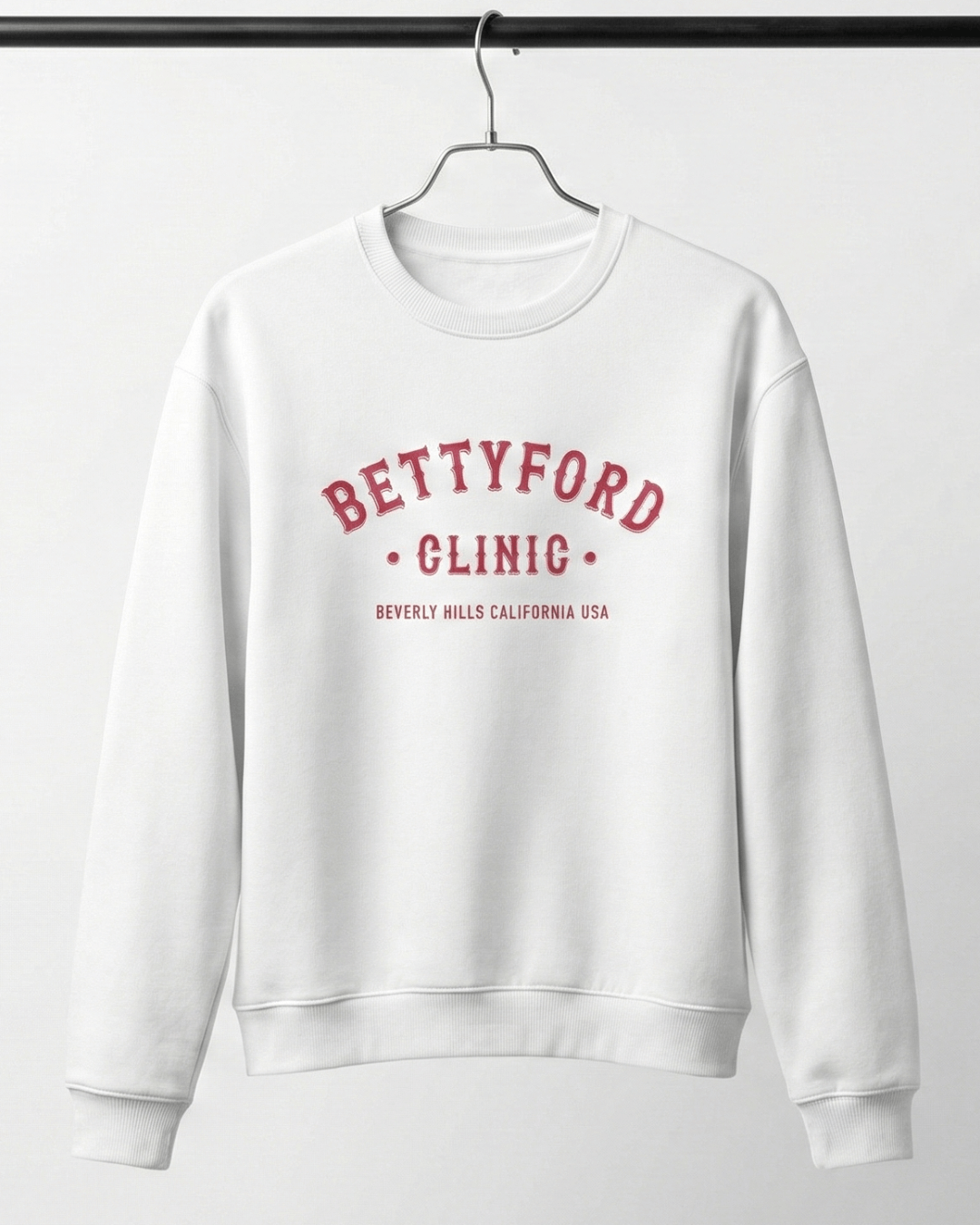 BETTY FORD CLINIC HEAVY SWEATER displayed on a hanger, featuring bold collegiate print in red on a white crewneck.