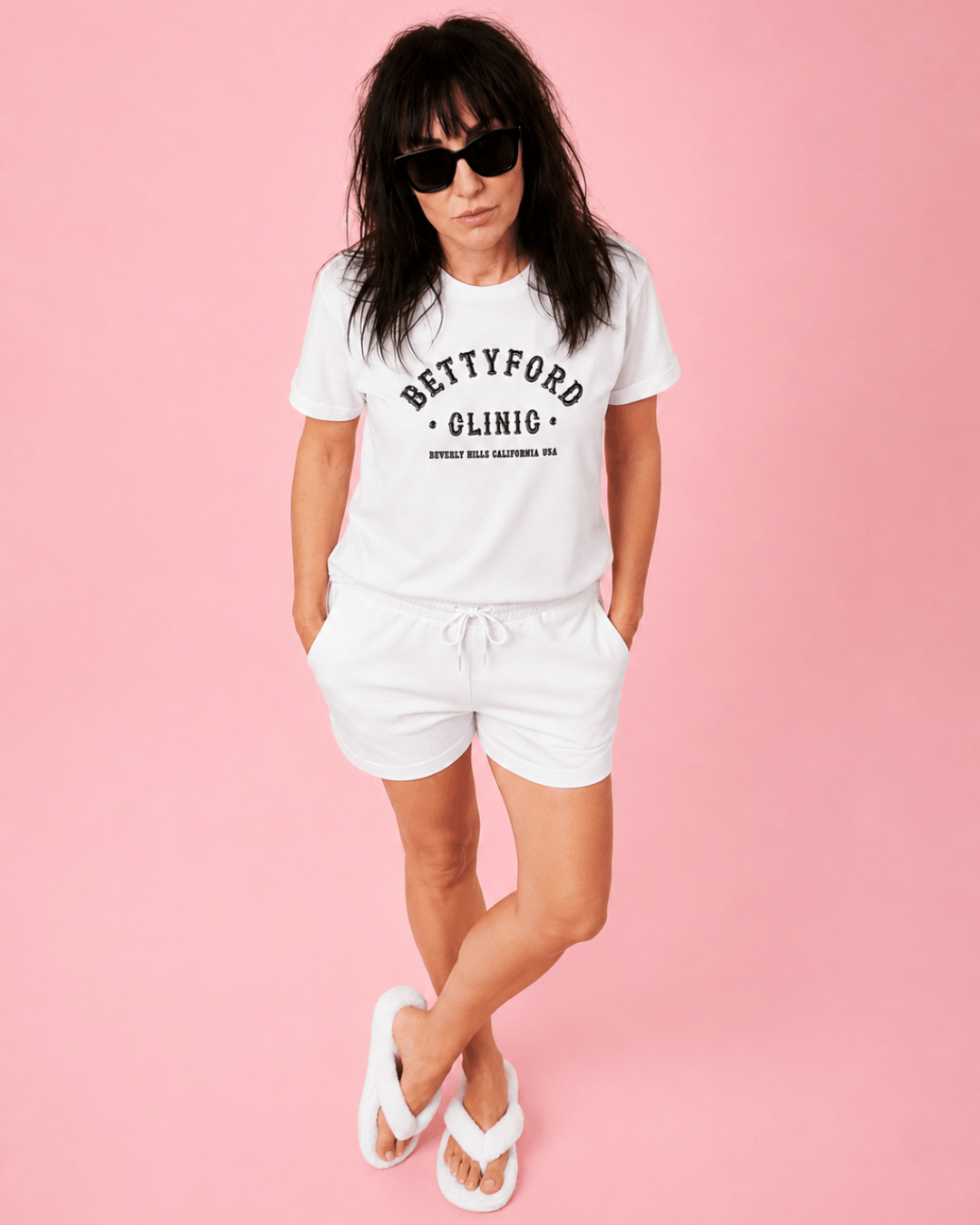 Lady wearing Betty Ford Clinic T-Shirt | Varsity Team in white, posing confidently with sunglasses.