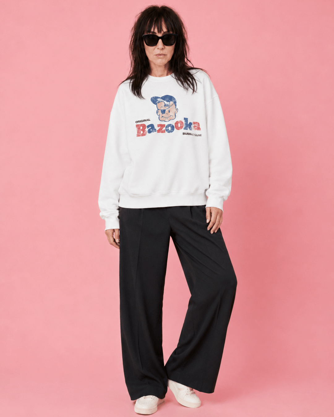 Woman wearing a Bazooka Joe Club Heavy Sweater standing against a pink background.