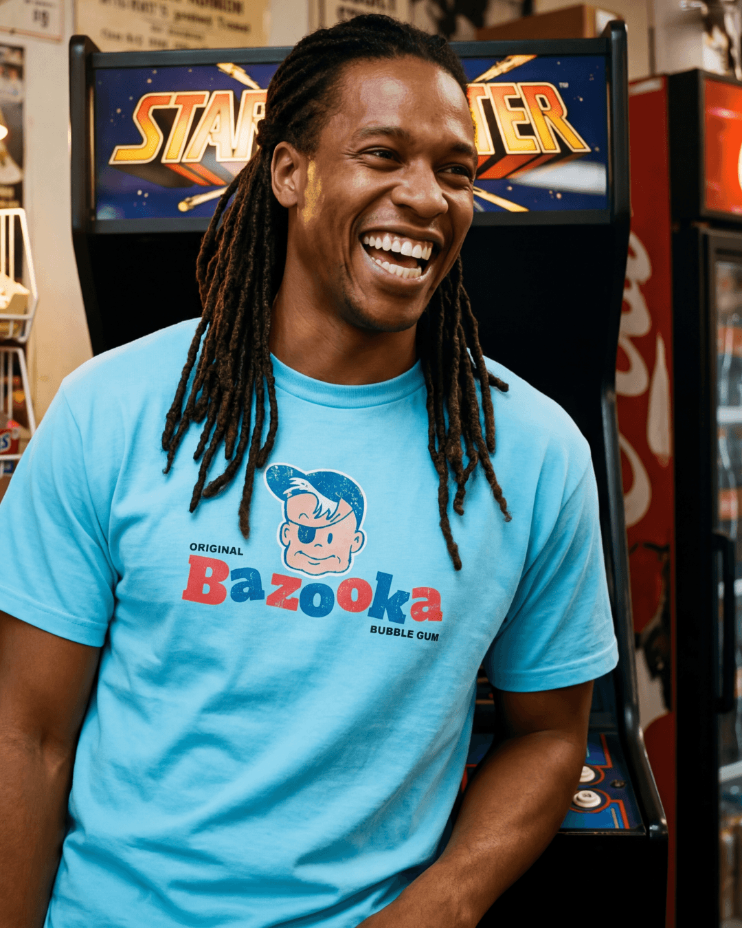 Man smiling wearing BAZOOKA JOE T-SHIRT | RETRO BUBBLEGUM LEGEND in front of an arcade machine.