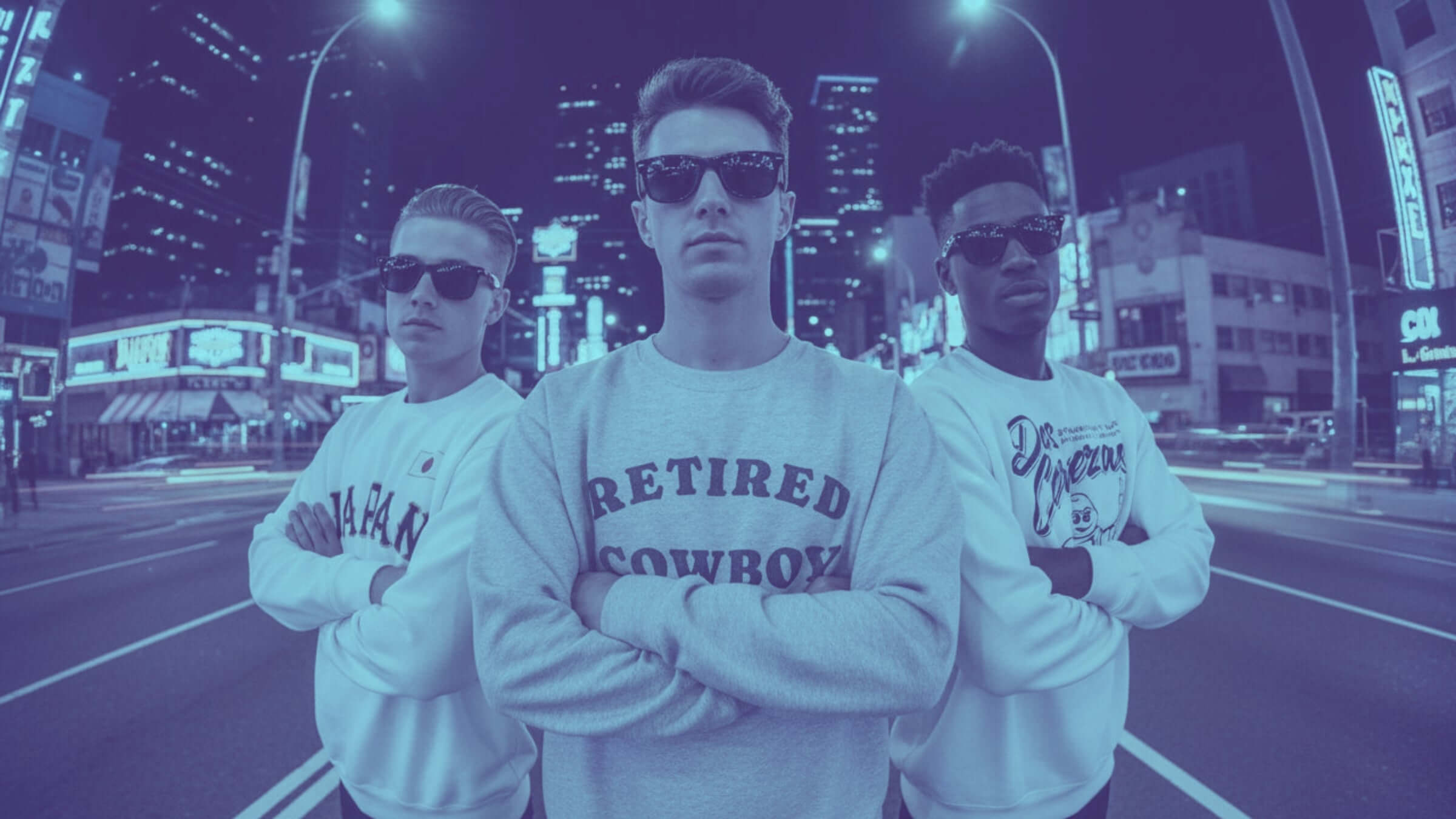 Three young men wearing stylish binky comfywear sweaters pose confidently on a city street at night.