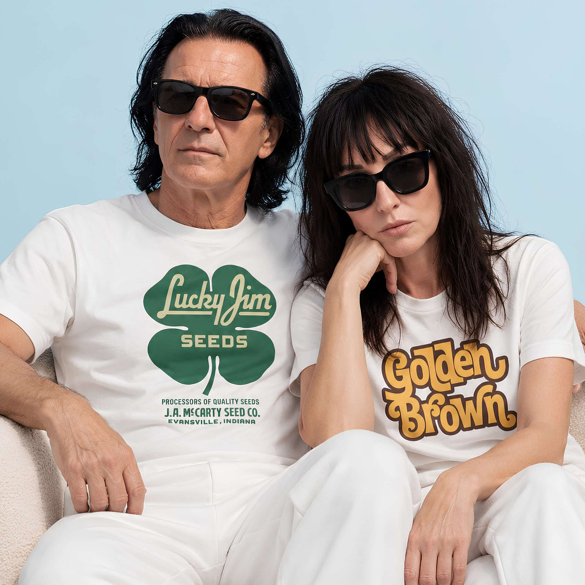 Stylish couple wearing retro t-shirts with 'Lucky Jim Seeds' and 'Golden Brown' designs, posing together casually.