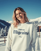 Smiling woman wearing HOTEL MIGRAINE HEAVY SWEATER in snowy outdoor setting, showcasing retro ski and streetwear style.