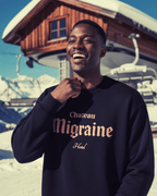 Model wearing HOTEL MIGRAINE HEAVY SWEATER in snowy ski resort backdrop, showcasing retro ski and streetwear style.