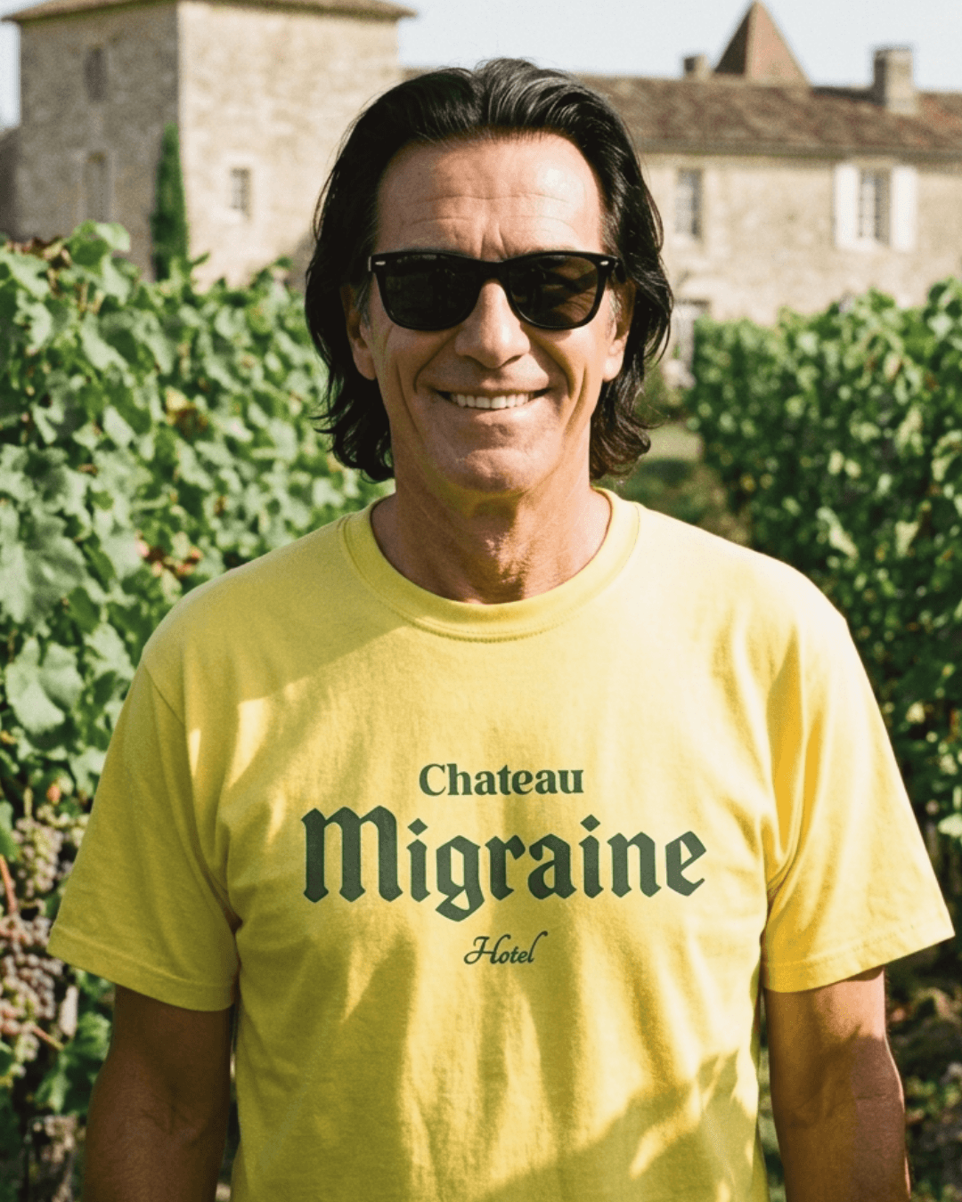 Man wearing a yellow Chateau Migraine T-shirt in a vineyard, exuding a fun and humorous vibe.