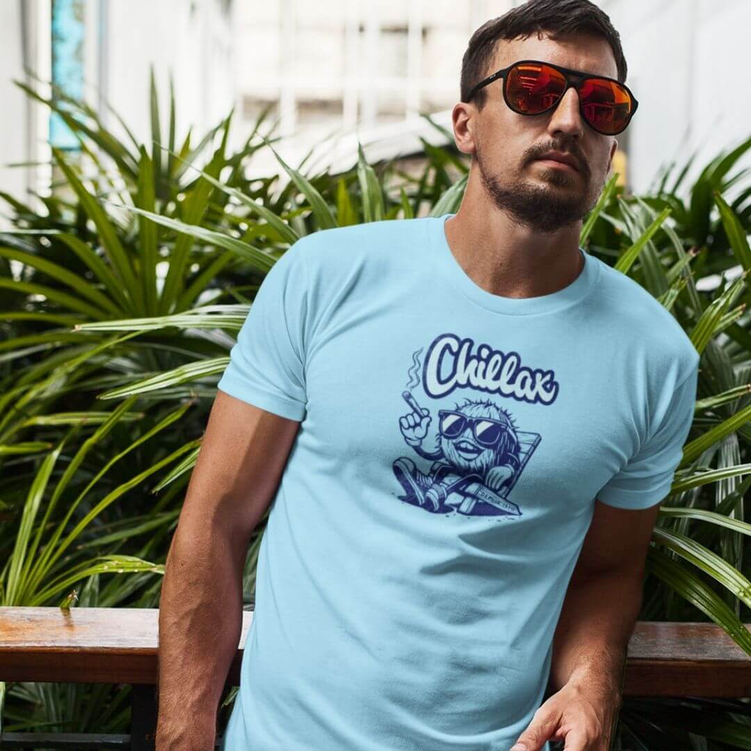 Man wearing a blue Chillax T-Shirt with a cool graphic, standing amidst lush green plants.