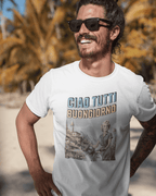 Man wearing Ciao Tutti T-shirt with design, smiling outdoors near palm trees.