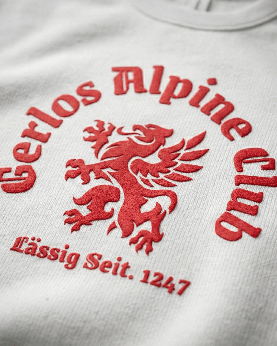 GERLOS ALPINE CLUB HEAVY SWEATER featuring an embroidered griffin crest and logo in red on a light background.