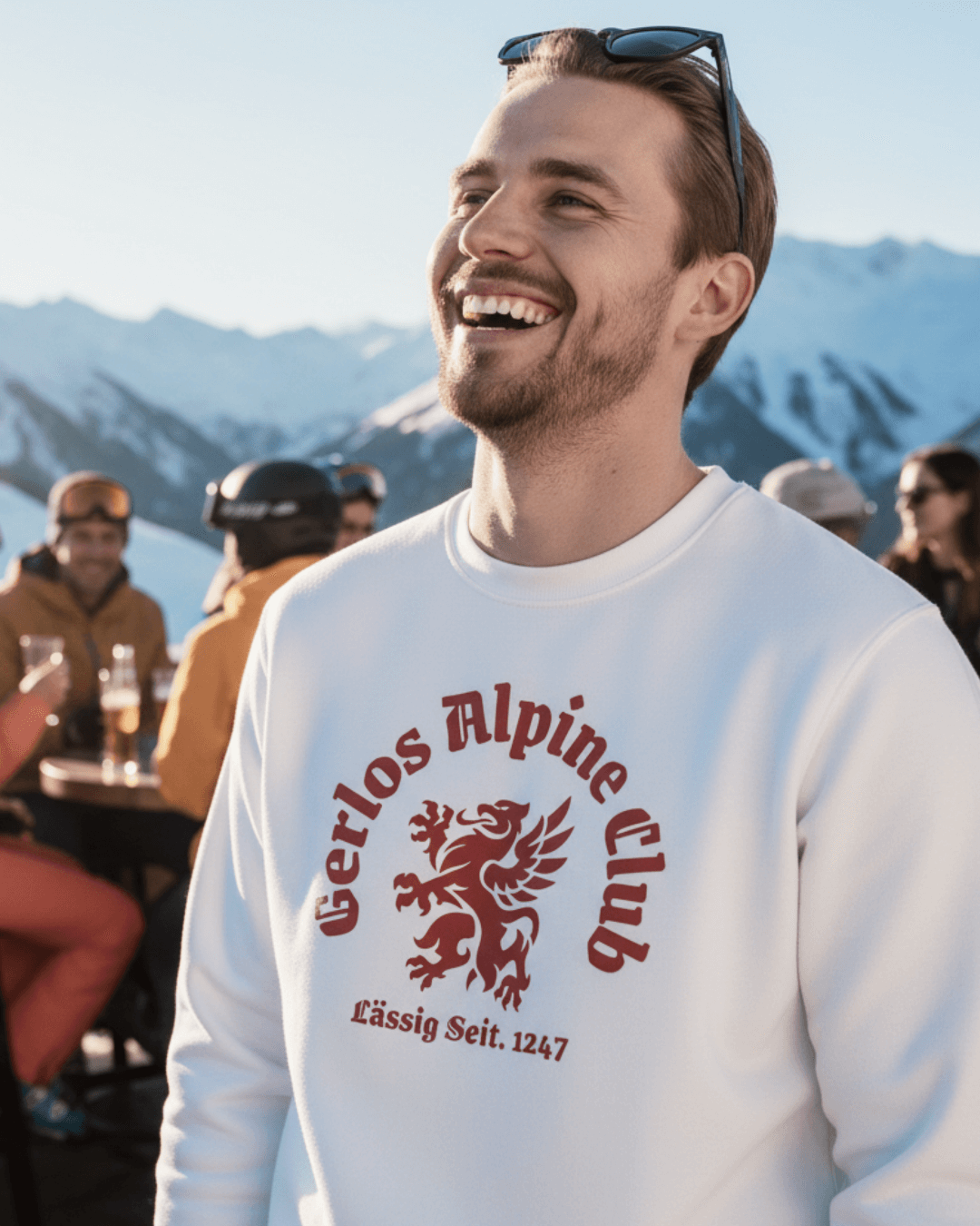 Young man smiling in GERLOS ALPINE CLUB HEAVY SWEATER with mountainous backdrop, perfect for après-ski style.