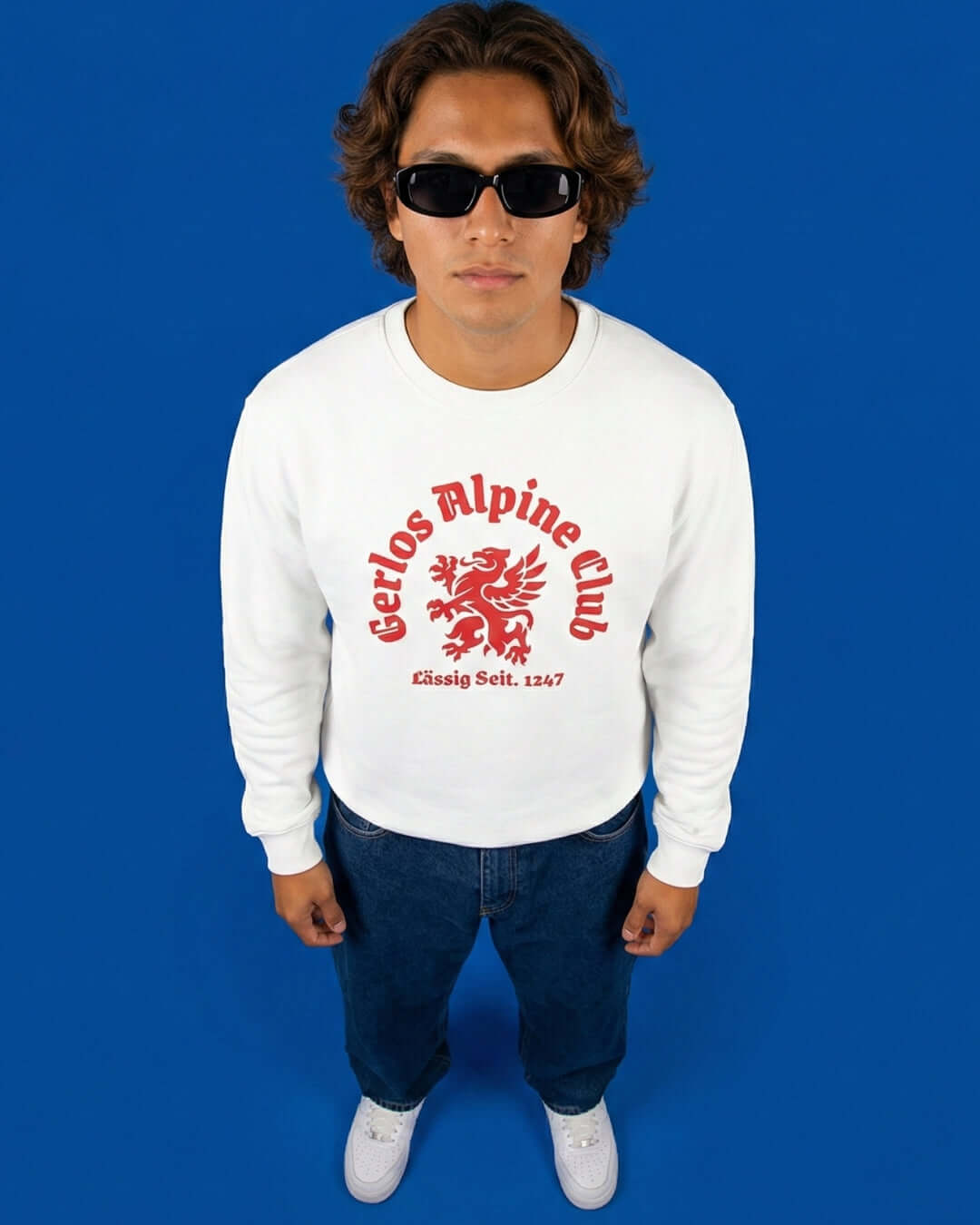 Model wearing GERLOS ALPINE CLUB HEAVY SWEATER with griffin crest on a blue background.