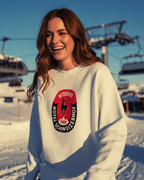 Woman smiling in a snowy landscape wearing HOTEL KITZBÜHEL HEAVY SWEATER with vintage hotel crest.