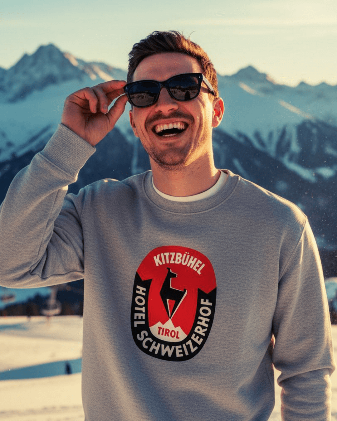 Man wearing HOTEL KITZBÜHEL HEAVY SWEATER with vintage hotel crest against alpine backdrop.