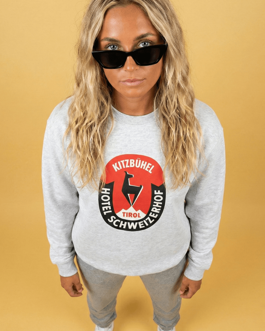Model wearing HOTEL KITZBÜHEL HEAVY SWEATER with vintage hotel crest and sunglasses.