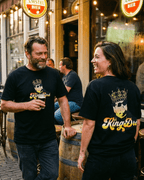 King Dre T-Shirt | Koning van het Levenslied worn by a couple enjoying drinks in a casual setting.