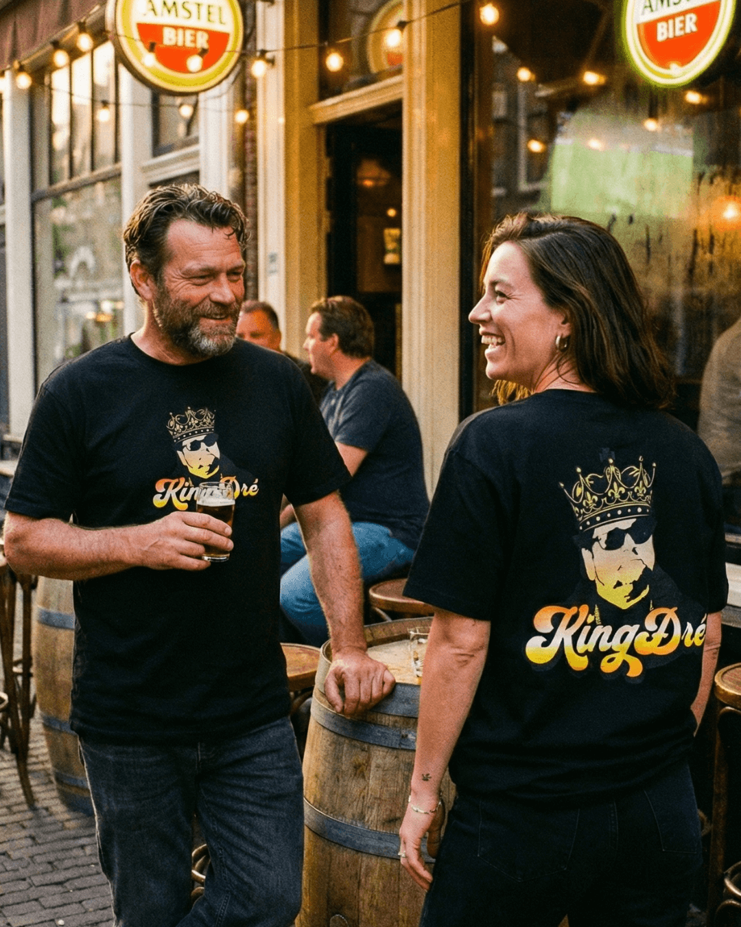 King Dre T-Shirt | Koning van het Levenslied worn by a couple enjoying drinks in a casual setting.