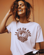 Woman smiling while wearing the La Vie En Rose T-shirt, showcasing a vintage design with floral elements.