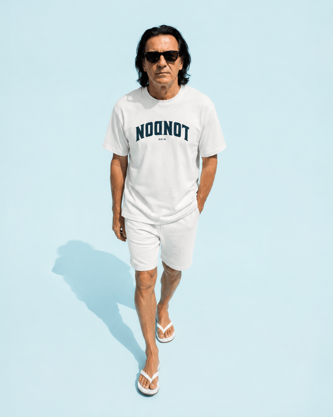 Man in white London Est. Ad 47 T-Shirt | Old City Varsity walking on aqua background.