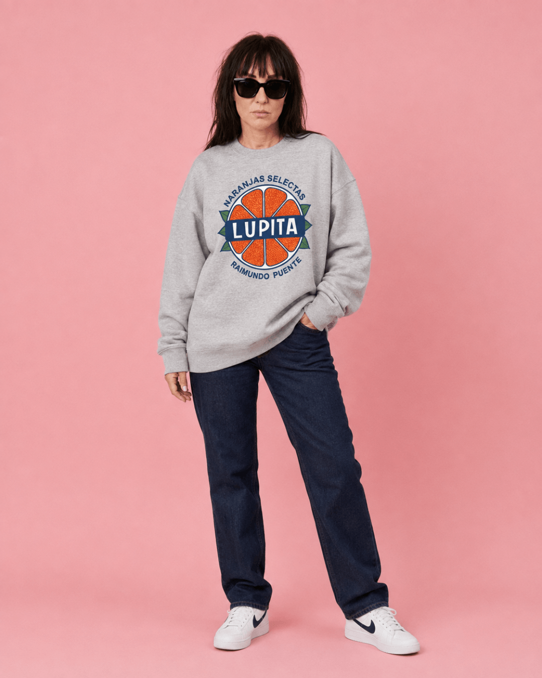 Lupita Naranjas Heavy Sweater worn by model with sunglasses against a pink background.