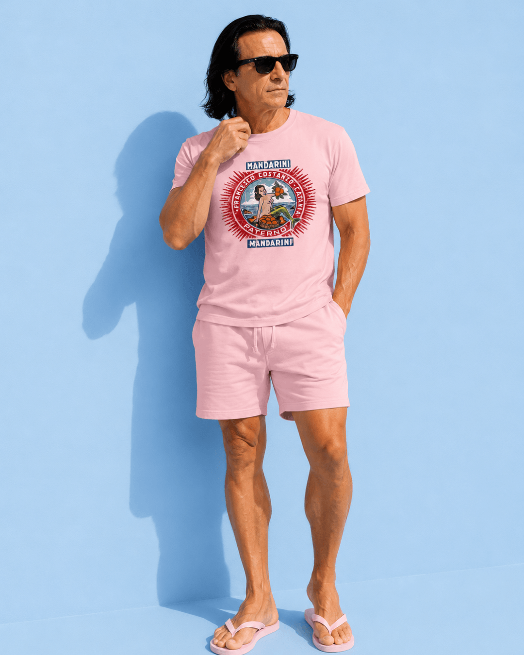 Man wearing Mandarini Catania T-Shirt | Sicilian Vintage, styled with sunglasses and casual shorts against a blue background.