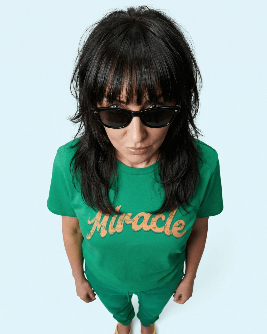 MIRACLE T-SHIRT | LUCK IS EARNED worn by a model with sunglasses, showcasing a vibrant green design.