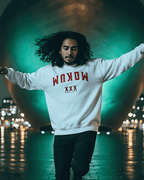 A model wearing a MOKUM EST 1300 SWEATER against a vibrant urban backdrop, showcasing its unique Amsterdam-inspired design.