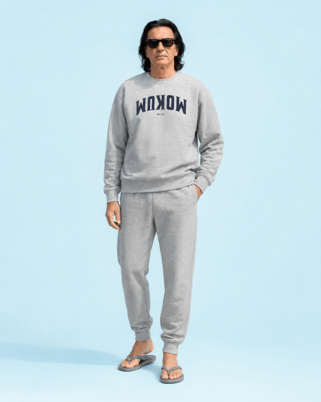 Mokum Est 1300 Heavy Sweater model wearing gray sweatshirt and sweatpants against a light blue background.