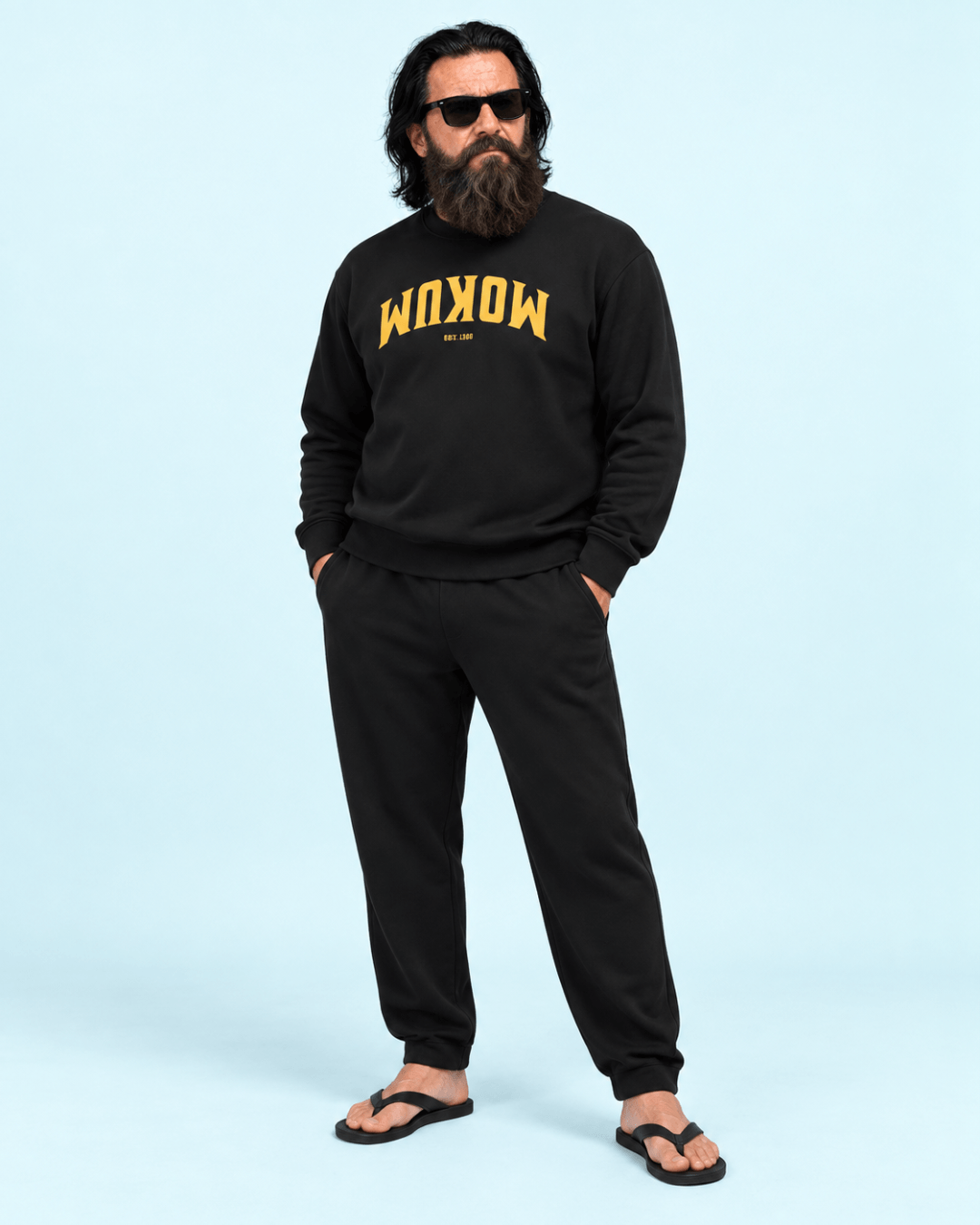 A man wearing a black Mokum Est 1300 Heavy Sweater and matching pants, posing casually in sunglasses.