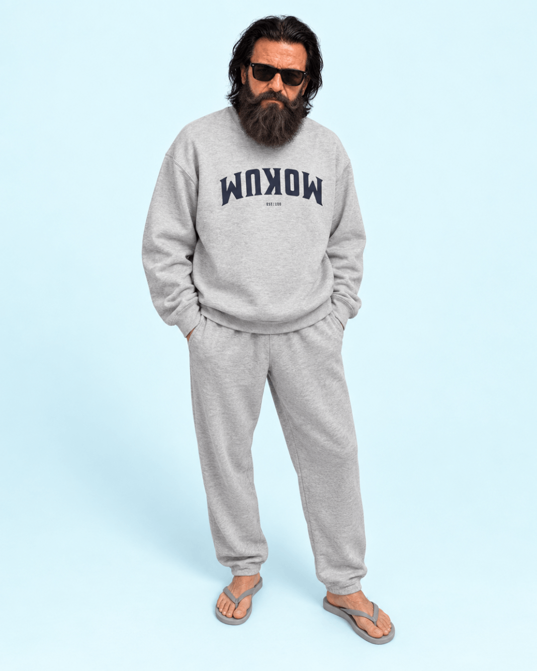 Mokum Est 1300 Heavy Sweater | Amsterdam Upside Down model wearing the sweater with gray pants against a light blue background.