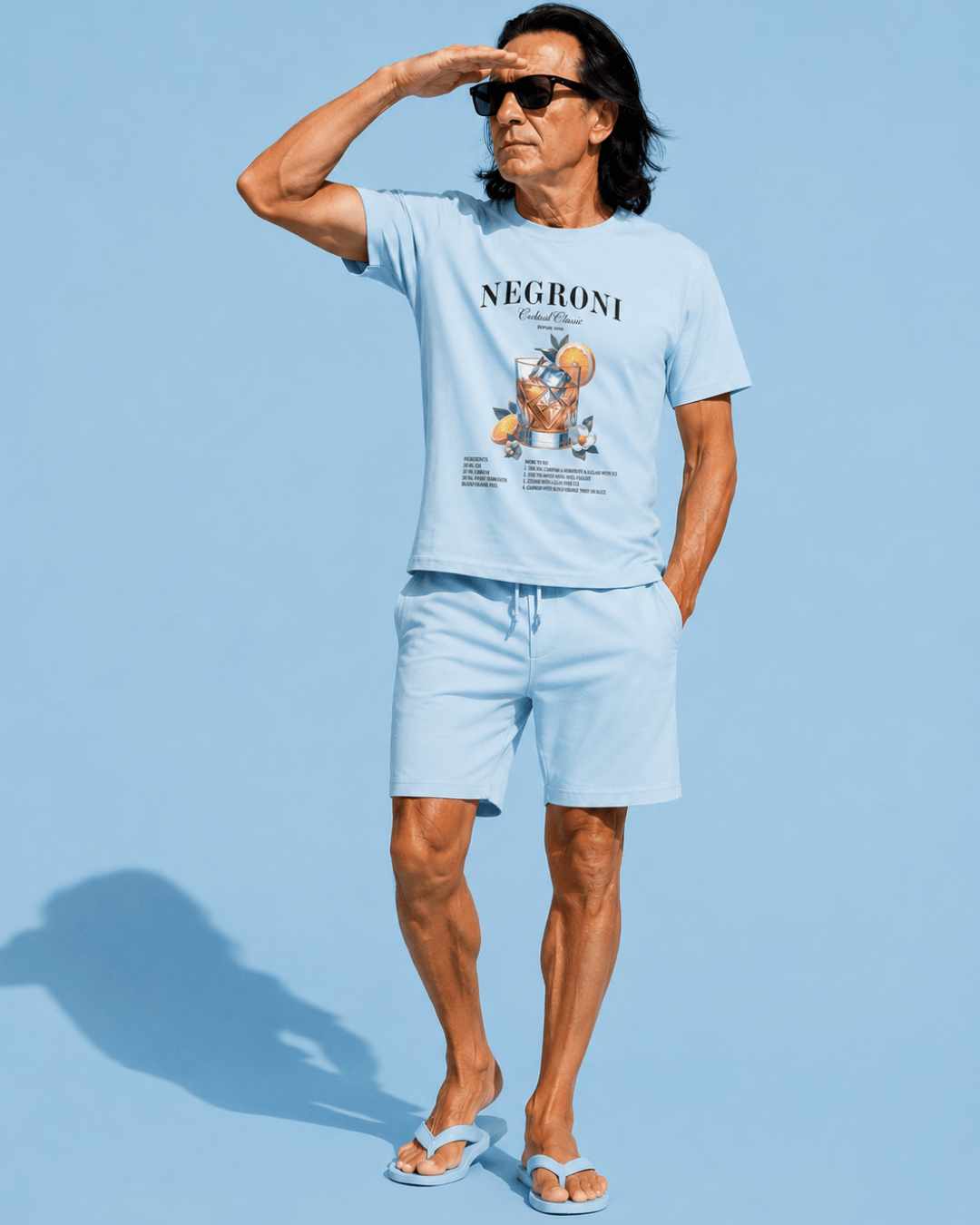 Man in blue Negroni T-shirt | Exquisite Luxury Edition standing confidently against a light blue background.