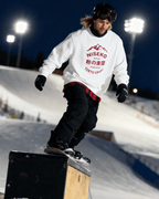 NISEKO POWDER PARADISE HEAVY SWEATER worn by a snowboarder performing tricks in a snowy terrain park at night.