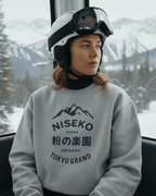 NISEKO POWDER PARADISE HEAVY SWEATER worn by a skier in a ski lift with snowy mountains in the background.