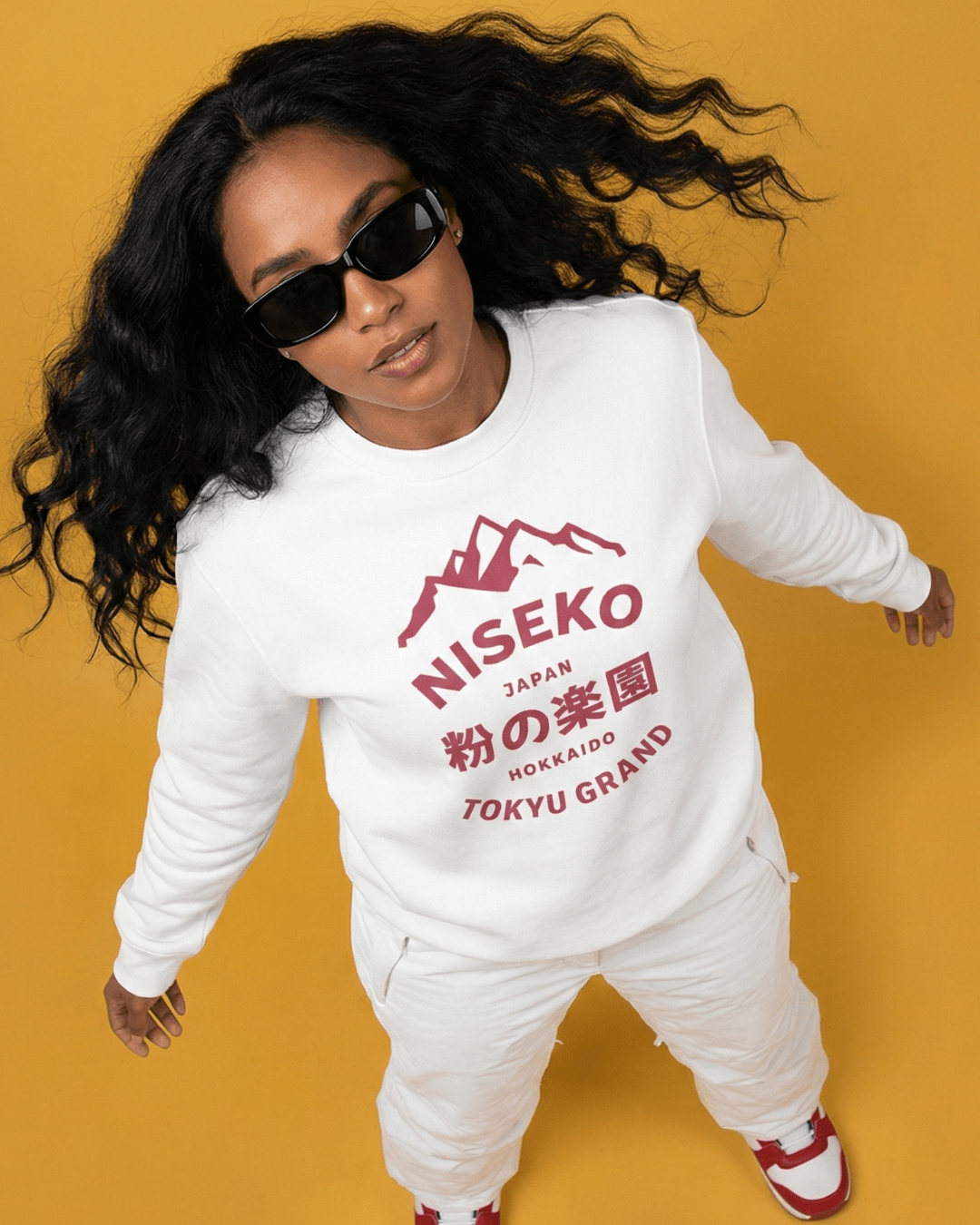 NISEKO POWDER PARADISE HEAVY SWEATER worn by a model against a yellow background with sunglasses.