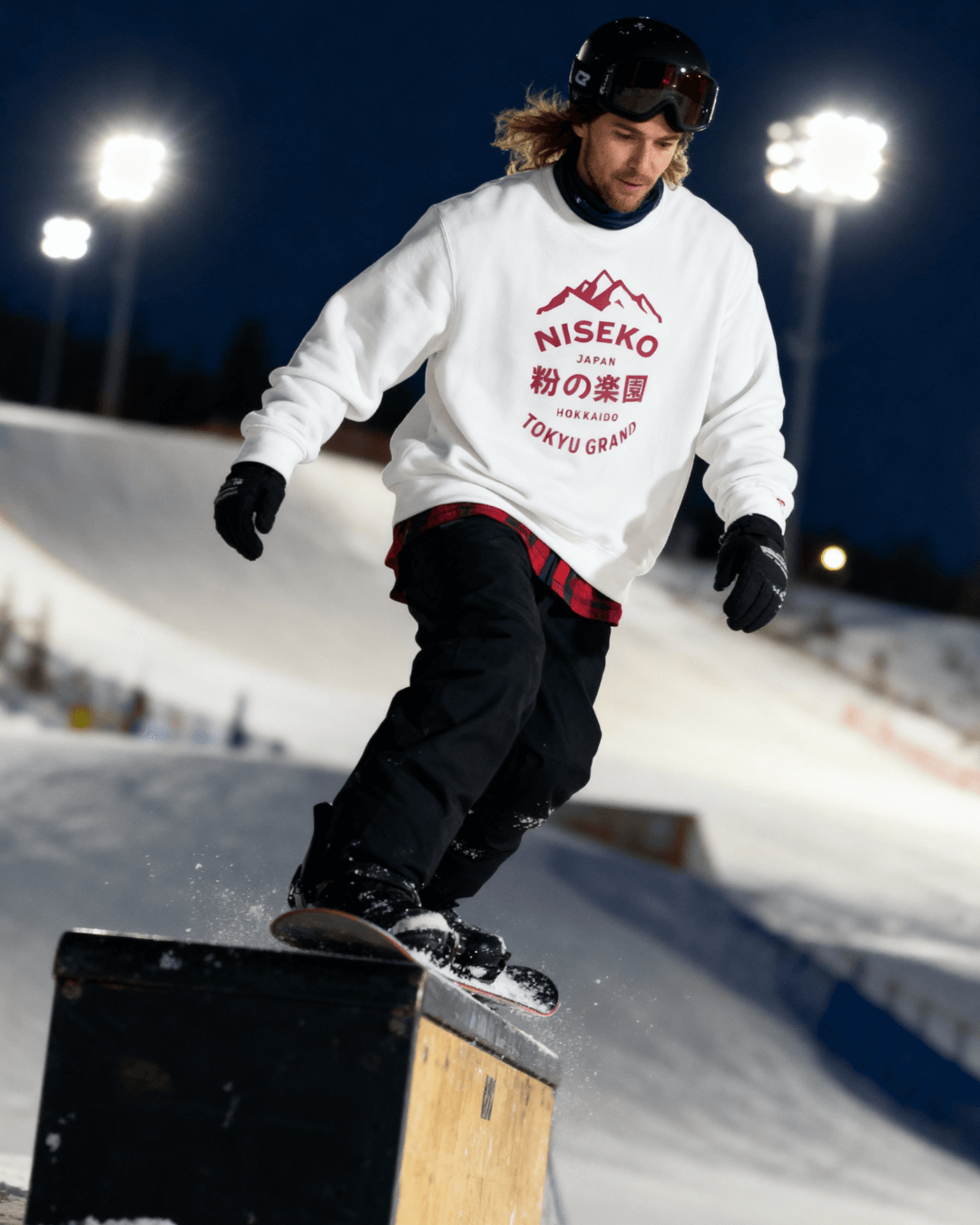 Person wearing a NISEKO POWDER PARADISE HEAVY SWEATER while snowboarding at night.