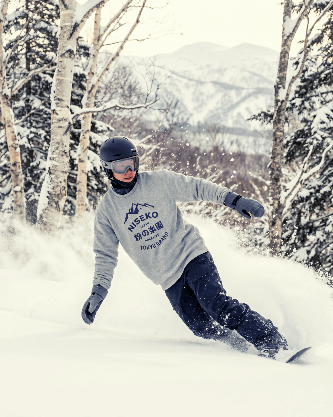 NISEKO POWDER PARADISE HEAVY SWEATER showcased by a snowboarder carving through powder snow in Niseko.