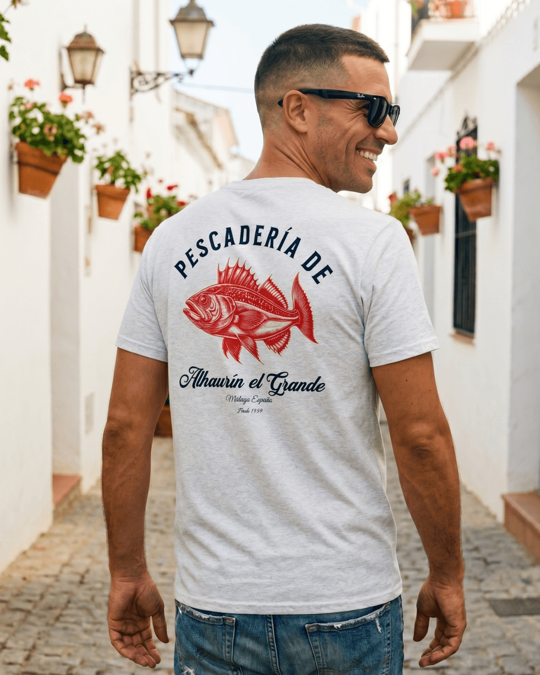 PESCADERIA T-SHIRT | ALHAURÍN EL GRANDE displayed on a man in a picturesque street.