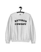 RETIRED COWBOY SWEATER displayed on a hanger, featuring a gray fabric with bold lettering.