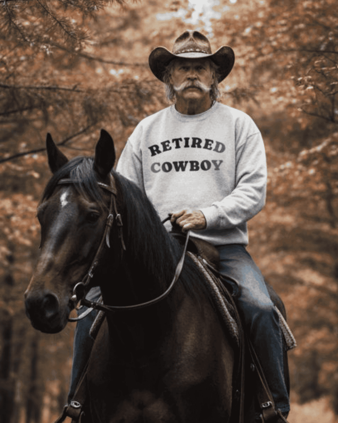 A man wearing a RETIRED COWBOY SWEATER riding a horse in a forest setting, showcasing binky comfywear and ultra-soft interior.