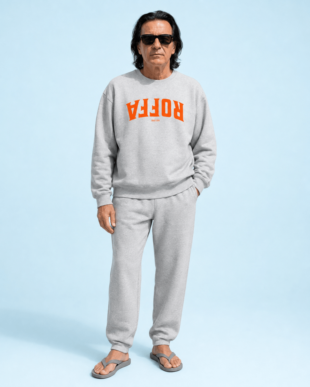 Man wearing Roffa 1340 Heavy Sweater in grey with orange print, posed against a light blue background.