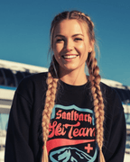 Young woman smiling in a Saalbach Ski Team Heavy Sweater, showcasing retro ski style and cozy unisex fit.
