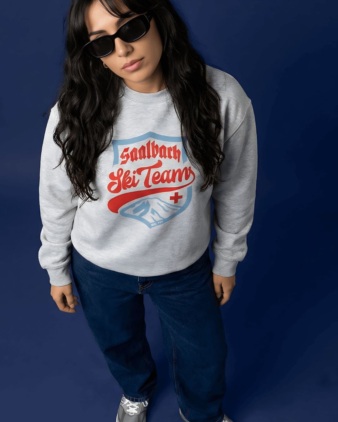 Saalbach Ski Team Heavy Sweater worn by a model with sunglasses against a blue background.