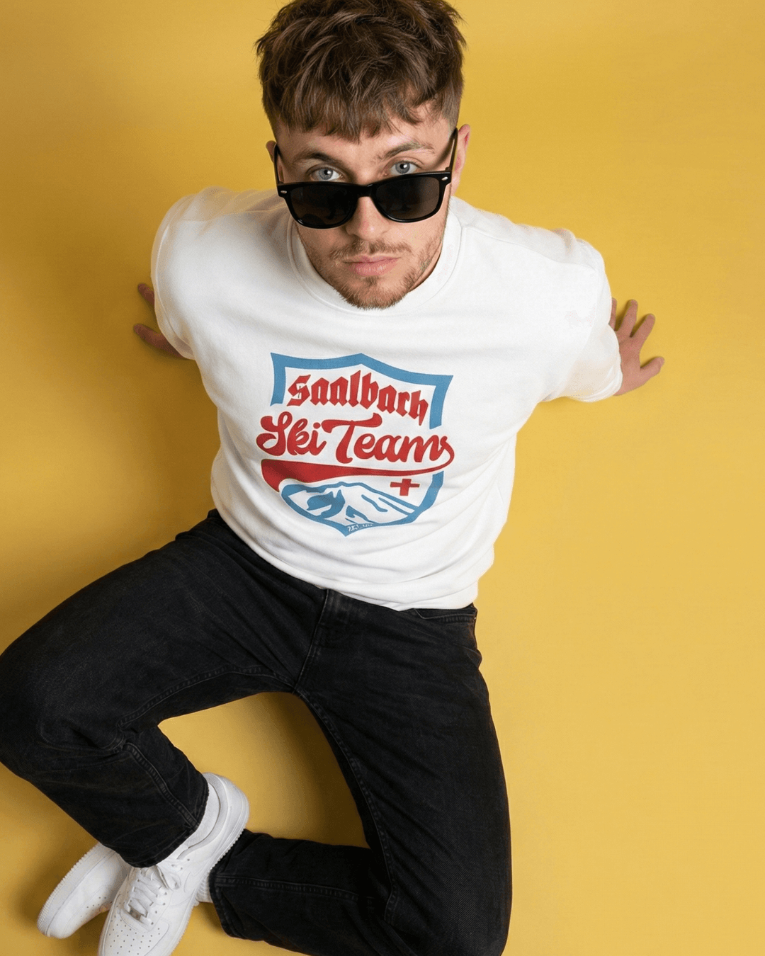 Saalbach Ski Team Heavy Sweater worn by a young man against a yellow background, showcasing a vintage ski team graphic.
