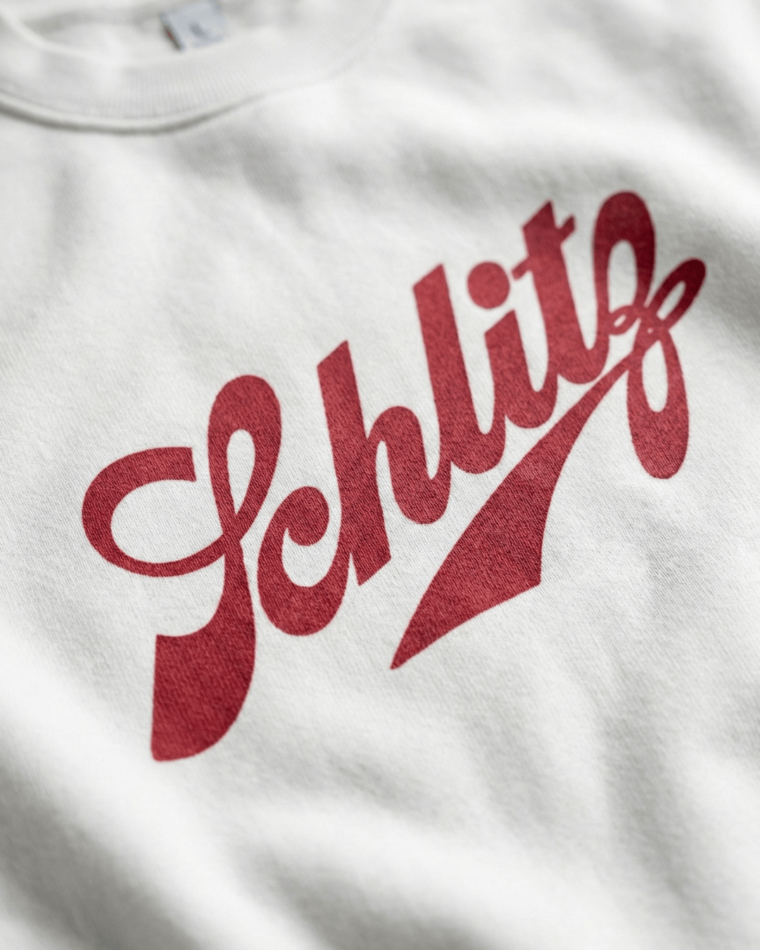 Close-up of the SCHLITZ HEAVY SWEATER logo in red typography on a white background.
