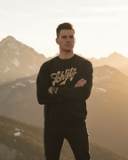 Man wearing SCHLITZ HEAVY SWEATER, showcasing vintage ski-lodge vibes against a mountain backdrop.
